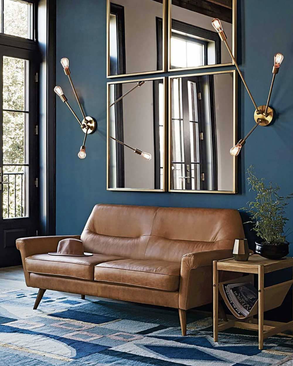 Canapé cuir style colonial dans salon lumineux avec miroir rectangle, lampes art déco et murs pétrole