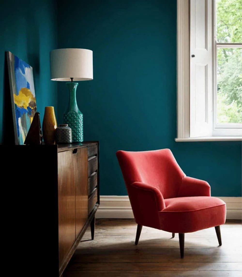 Salon de style vintage avec murs bleu pétrole et fauteuil rouge velours